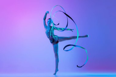 Portrait of one young rhythmic gymnast posing with ribbon in her hand isolated on pink purple background in neon light. Concept of action, motion, sport life, motivation, competition. Copyspace for ad