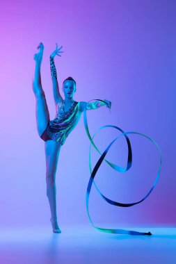 Portrait of tender young girl standing on twine with ribbons, posing isolated on pink purple background in neon light. Concept of action, motion, sport life, motivation, competition. Copyspace for ad