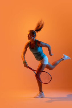 Sportive woman, professional tennis player ion action, training isolated over orange studio background in neon light. Concept of sport, health, strength, motion, hobby, lifestyle. Copy space for ad