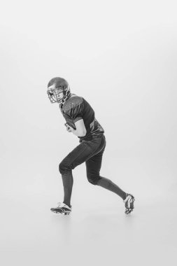 Portrait of concentrated young man, american football player in motion, action. Black and white photography. Centre-back. Concept of sport, retro style, 20s, fashion, action, college sport, youth