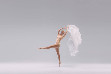 Portrait of young tender ballerina dancing with transparent white fabric isolated over grey studio background. Classic performance. Concept of classic ballet, inspiration, beauty, dance, creativity
