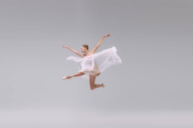 Portrait of young ballerina dancing with transparent fabric isolated over grey studio background. Flying like butterfly. Concept of classic ballet, inspiration, beauty, dance, creativity