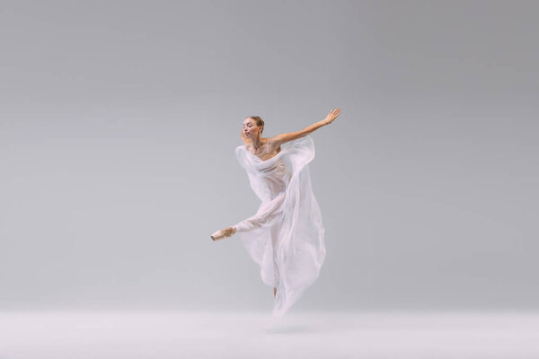 Portrait of young artistic ballerina dancing with transparent fabric isolated over grey studio background. Flexibility. Concept of classic ballet, inspiration, beauty, dance, creativity