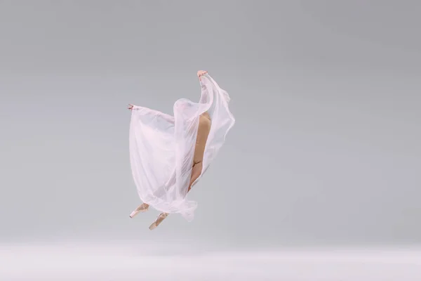 Portrait of young ballerina dancing, performing in beige cloth, covered with fabric isolated over grey studio background. Concept of classic ballet, inspiration, beauty, dance, creativity