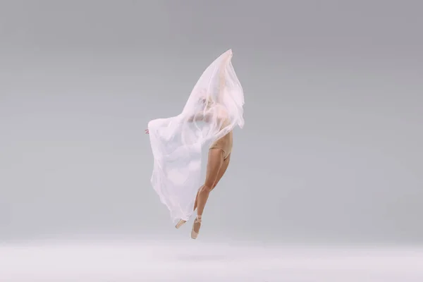 Portrait of young ballerina covered with transparent fabric, isolated over grey studio background. Flight of tenderness. Concept of classic ballet, inspiration, beauty, dance, creativity