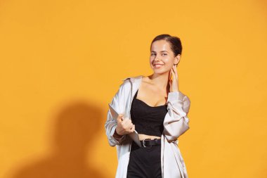 Portrait of young cheerful woman in casual clothes posing with tablet isolated over yellow studio background. Concept of business, lifestyle, youth, emotions, facial expression, ad