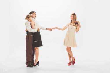 Portrait of young man hugging woman and giving hand to another girl. Flirty relationship. Faith and betrayal. Concept of retro fashion, style, youth culture, emotions, relationship, party, ad