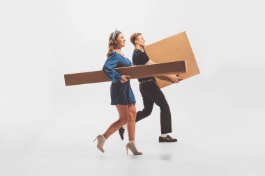 Young man and woman carrying big cardboard boxes isolated over white background. Black Friday shopping, sales, moving. Concept of retro fashion, style, youth culture, emotions, relationship, ad