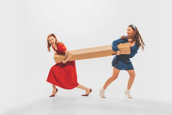 Portrait Two Stylish Beautiful Girls Pulling Big Cardboard Box Isolated — Stockfoto