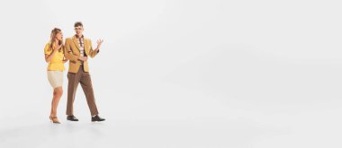 Portrait of young couple, man and woman lively talking discussing while walking isolated over white studio background. Concept of retro fashion, style, youth culture, emotions, relationship, ad