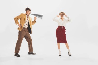 Portrait of young man in yellow jacket shouting at stylish woman in megaphone isolated over white background. Big sales, expressive news. Concept of retro fashion, style, youth culture, emotions, ad