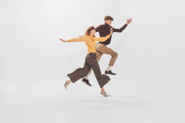 Portrait of young man and woman in stylish clothes posing in a jump isolated on white studio background. Autumn fashion collection. Concept of retro fashion, style, youth culture, emotions, beauty, ad