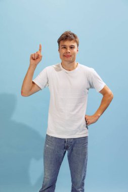 Portrait of young man in casual clothes, posing, rising finger , having new idea isolated over blue background. Generating ideas. Concept of emotions, facial expression, lifestyle, fashion, youth