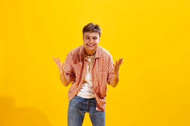 Portrait of young man in checkered shirt posing with happy and excited expression isolated over yellow studio background. Greetings. Concept of emotions, facial expression, lifestyle, fashion, youth