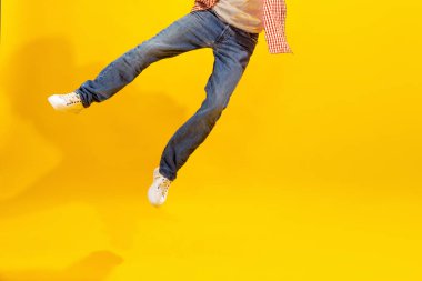 Cropped image of male legs in jeans and white sneakers isolated over yellow studio background. Uncertainty. Concept of emotions, facial expression, lifestyle, fashion, youth