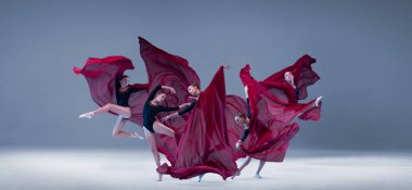 Portrait of young ballerina dancing with deep red clored fabric isolated over blue grey studio background. Passion art. Concept of classic ballet, inspiration, beauty, dance, creativity