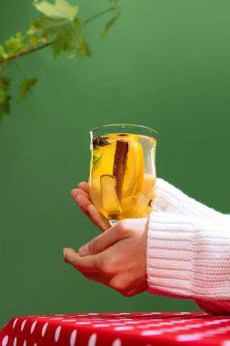 Teacupwith delicious herbal tea with citrus, lemons, ginger and mint isolated over green background. Vitamins. Concept of taste, drink, healthy ingredients, seasonal drink. Copy space for ad