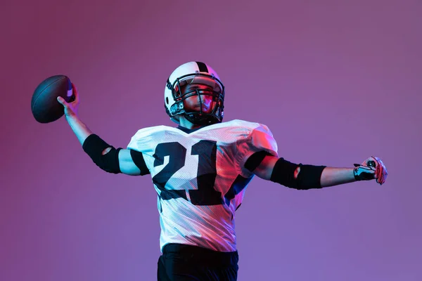 Portrait of american football player in motion, throwing ball in isolated over purple background in neon light. Active player. Concept of team game, energy, sport, competition. Copy space for ad