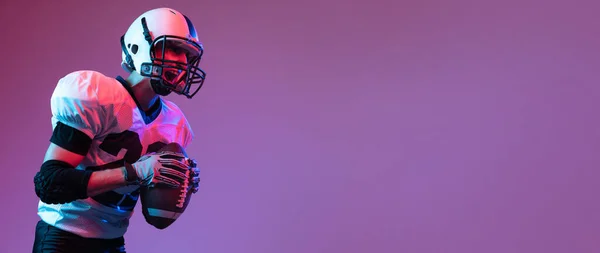 Portrait of professional american football player shouting before game to rise team spirit isolated over purple background neon light. Concept of active life, team game, energy, sport, competition.