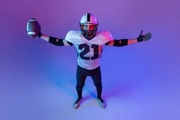 Top view portrait of man, american football player training isolated over purple background in neon light. Champion. Concept of active life, team game, energy, sport, competition. Copy space for ad