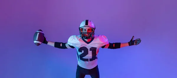 Top view portrait of man, american football player posing isolated over purple background in neon light. Winner. Concept of active life, team game, energy, sport, competition. Copy space for ad