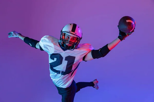 Top view portrait of man, american football player training, throwing ball isolated on purple background in neon light. Concept of active life, team game, energy, sport, competition. Copy space for ad