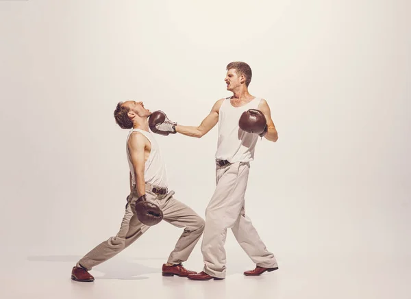 Portrait of two men playing, boxing in gloves isolated over grey studio background. Fighting with opponent. Concept of sport, hobby, work, active lifestyle, retro fashion. Copy space for ad