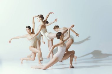 Group of young women, ballerinas dancing, performing isolated over grey studio background. Attraction of choreography. Concept of art, beauty, aspiration, creativity, classic dance style, elegance
