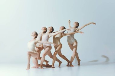Group of young girls, ballet dancers performing isolated over grey studio background. Expression of freedom. Concept of art, beauty, aspiration, creativity, classic dance style, elegance