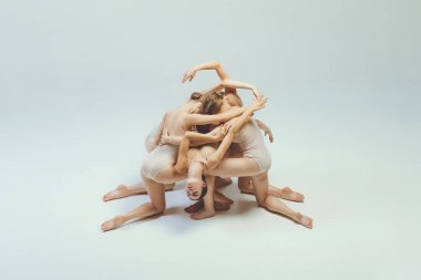 Group of young girls, ballet dancers performing, posing isolated over grey studio background. Pyramid pose. Concept of art, beauty, aspiration, creativity, classic dance style, elegance