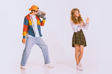 Portrait of stylish young man in trendy colorful jacket with music player posing with beautiful girl isolated on grey background. Dating. Concept of youth, retro style, 90s era, fashion, lifestyle, ad