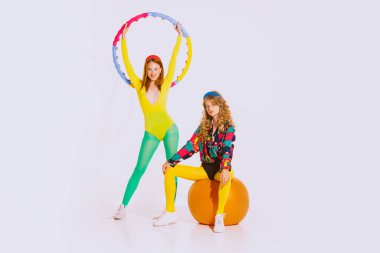 Portrait of stylish young girls in bright clothes doing fitness, posing isolated over grey background. Healthy lifestyle. Concept of youth, retro style, 90s era, fashion, lifestyle, ad