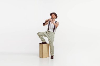Portrait of young man playing clarinet isolated over white studio background. Countryside singer performing. Concept of live music, performance, retro style, creativity, artistic lifestyle