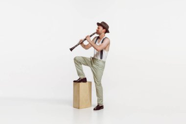Portrait of young man playing clarinet isolated over white studio background. Expressive performance. Concept of live music, performance, retro style, creativity, artistic lifestyle