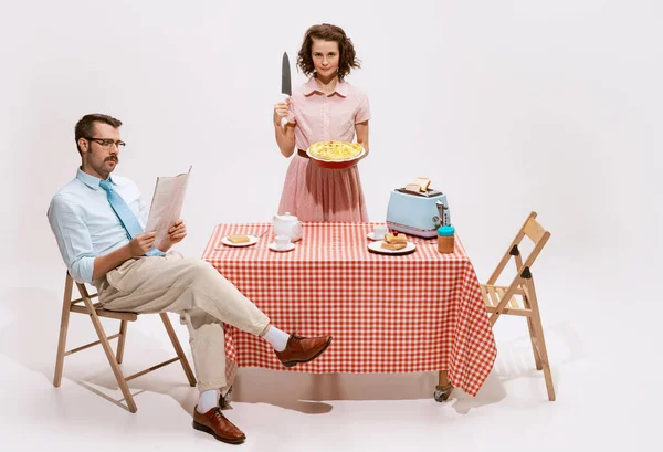 Portrait of couple sitting at the table, having breakfast isolated on white background. Woman with knife. Movie remake. Love, relationship, retro style, creativity, family concept. Copy space for ad