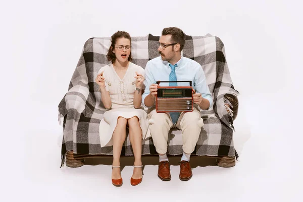 Portrait of couple sitting on sofa and listening to the radio. Woman singing and dancing. Concept of love, relationship, retro style, creativity, family. Copy space for ad