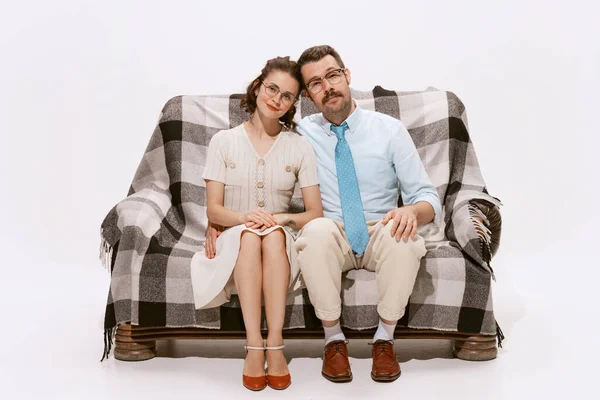 Portrait of beautiful couple, man and woman sitting on sofa and looking at camera isolated over white background. Concept of love, relationship, retro style, creativity, family. Copy space for ad