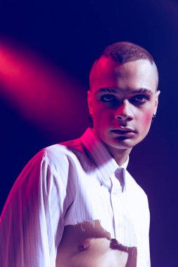 Makyaj yapan genç bir adamın yakın plan portresi, dumanlı gözler, neon ışıkta mor arkaplanda izole edilmiş poz. Moda kavramı, seçim özgürlüğü, yaşam tarzı, lgbt, Z nesli, trendler