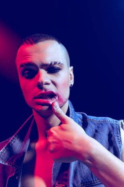 Makyaj yapan genç bir adamın yakın plan portresi, dumanlı gözler, neon ışıklı karanlık arka planda izole edilmiş pozlar. Gayriresmi. Moda kavramı, seçim özgürlüğü, yaşam tarzı, lgbt, Z nesli, trendler