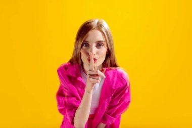 Sarı stüdyo arka planında izole edilmiş parmak ağıza poz veren güzel bir kadının portresi. Sessiz kalmak. Güzellik kavramı, yaşam tarzı, gençlik, duygular, yüz ifadesi, reklam.
