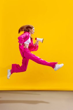 Sarı stüdyo arka planında izole edilmiş megafonla sıçrayışta poz veren güzel bir kadının portresi. Güzellik kavramı, yaşam tarzı, gençlik, duygular, yüz ifadesi, reklam.