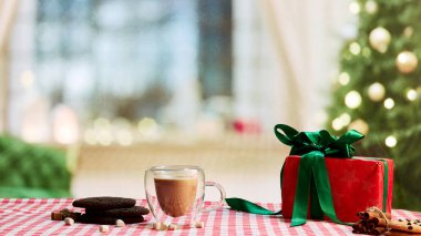 Sütlü, çikolatalı kurabiyeli ve tarçınlı bir fincan lezzetli kahve. Sıcak içecekler, tat, kış, rahatlık kavramı. Işıkları ve Noel ağacı olan güzel bir tatil geçmişi