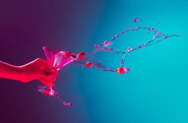 Kadın eli, pembe neon ışıkta martini kokteylinin üzerine sıçrıyor. Gece hayatı, parti. Sert bir içki. Alkollü içki, parti, zevk anlayışı. Yiyecek ve içecek sanatı