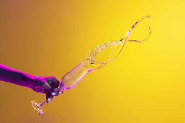 Sarı zemin üzerinde pembe neon ışıkta izole edilmiş bir şekilde şampanyanın üzerine kadın eli dökülüyor. Böğürtlen. Alkollü içki, parti, zevk anlayışı. Yiyecek ve içecek sanatı. İlan için alanı kopyala