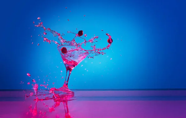 Martini cocktail splash over blue background in pink neon light. Nightlife, party. Splitting drink. Concept of alcoholic drinks, party, taste. Food and drink art