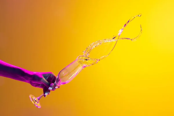 Female hand spilling over champagne isolated over yellow background in pink neon light. Berry taste. Concept of alcoholic drinks, party, taste. Food and drink art. Copy space for ad