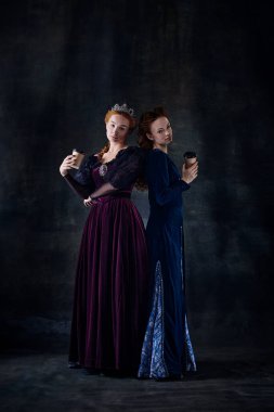 Karanlık arka planda izole edilmiş kraliçeler gibi duran iki güzel kadının portresi. Kahve molası. Kraliyet ailesi. Devir, modernlik ve rönesans kavramı, barok tarzı, güzellik, tarih