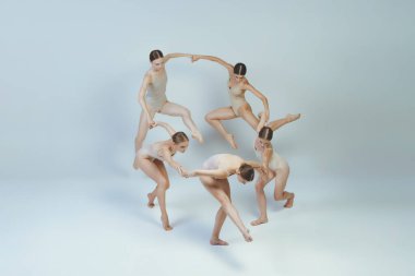 Group of young girls, ballet dancers performing, posing isolated over grey studio background. Dancing in a cricle. Concept of art, beauty, aspiration, creativity, classic dance style, elegance