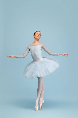 Mavi stüdyo arka planında soyutlanmış bir şekilde dans eden genç balerin portresi. Klasik dansın güzelliği. Klasik bale kavramı, ilham, güzellik, dans, yaratıcılık