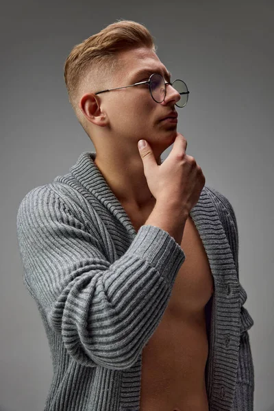 ニットのセーターと眼鏡を身に纏った筋肉質の肉体を持つ残忍な青年の肖像画がグレーのスタジオの背景に隔離されている 男性の健康の概念 自然の美しさ ボディ スキンケア — ストック写真